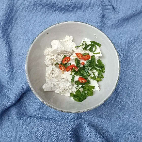 Haluskan tahu. Masukkan cabai rawit dan daun bawang.