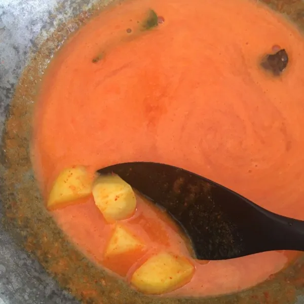 Tuang air ke dalam wajan, lalu tambahkan bumbu halus, asam kandis, daun jeruk. Masukkan kentang dan nyalakan kompor dengan api sedang cenderung kecil lalu masak hingga mendidih.