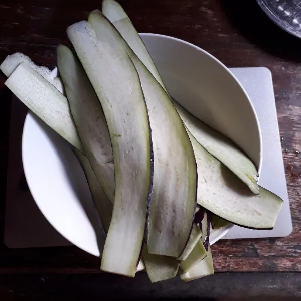 Iris tipis memanjang terong, rendam dengan air garam selama 20 menit, cuci bersih dan tiriskan.