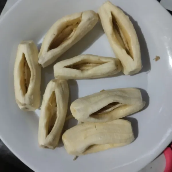 Kupas pisang lalu belah tengahnya jangan sampai putus. Tekan-tekan perlahan.