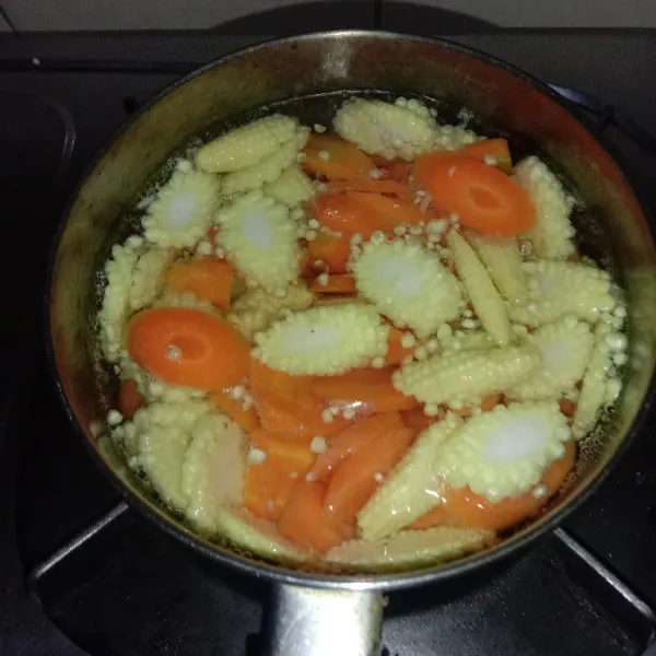 Masak air hingga mendidih lalu masukkan wortel dan jagung muda, beri sedikit garam, masak hingga setengah matang.