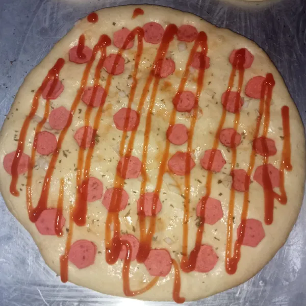 Gilas adonan bentuk bulat kemudian tambahkan topping olesan saus tomat, potongan sosis, bawang bombay, saus tomat dan mayonaise, diamkan selama 20 menit.