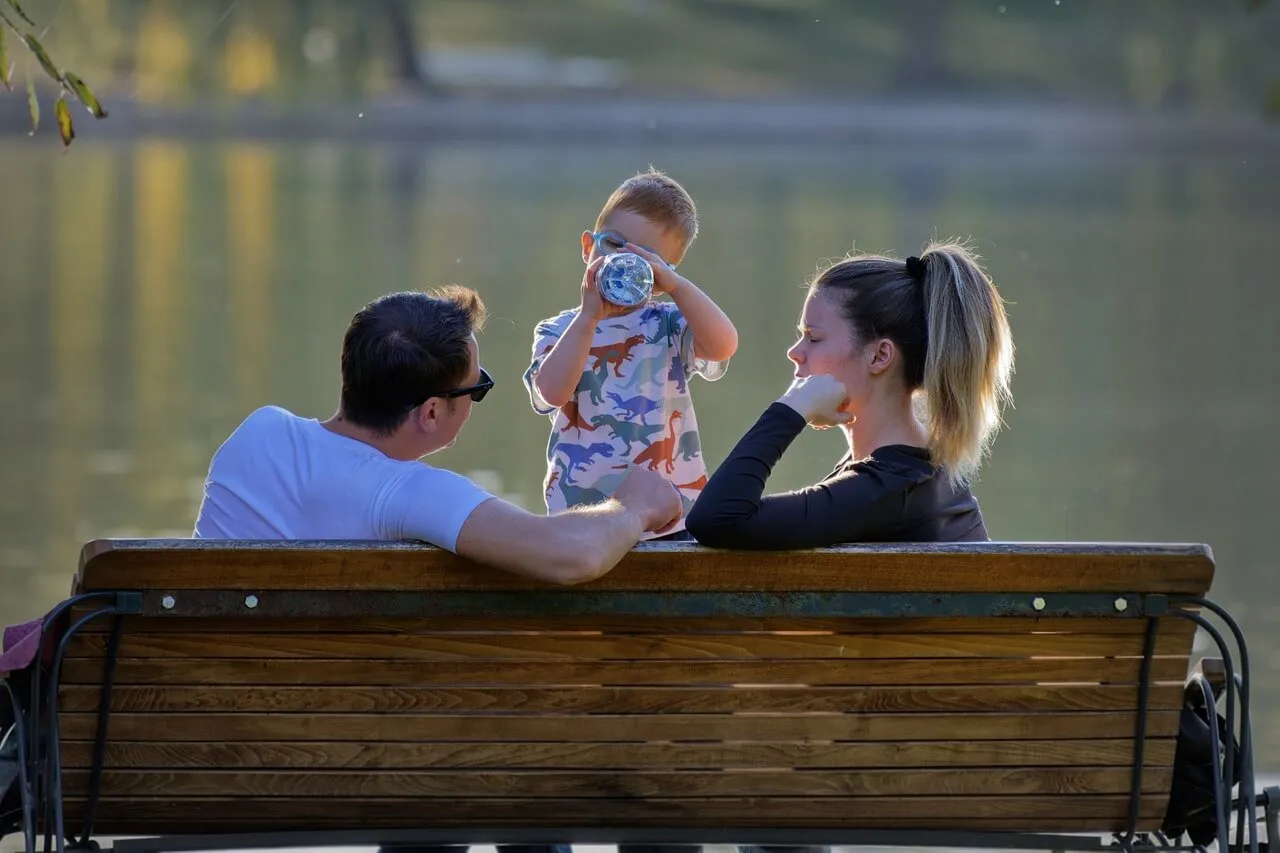 Bayi sedang minum susu di pinggir danau bersama orang tua