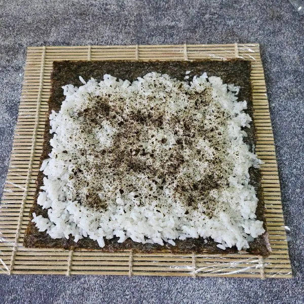 Tata nori di atas sushi matt, beri nasi secukupnya lalu ratakan. Taburi dengan nori bubuk.