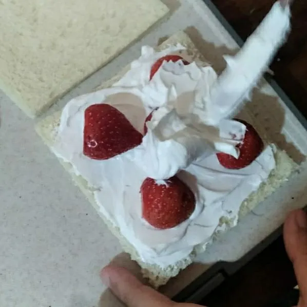 Tata strawberry, letakkan tepat di tengah secara diagonal serta di samping. Timpa lagi dengan whipped cream sampai rata.