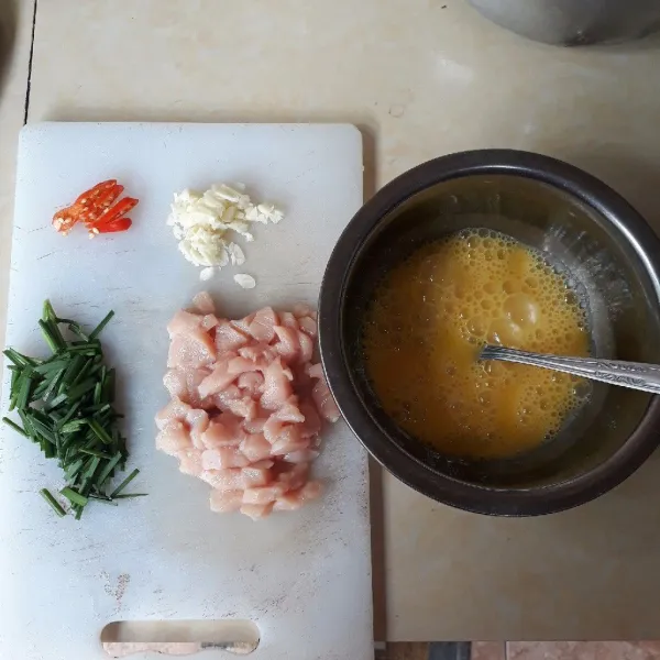 Kocok lepas telur. Cincang bawang putih, iris cabai, dan daun kucai, potong dadu ayam.