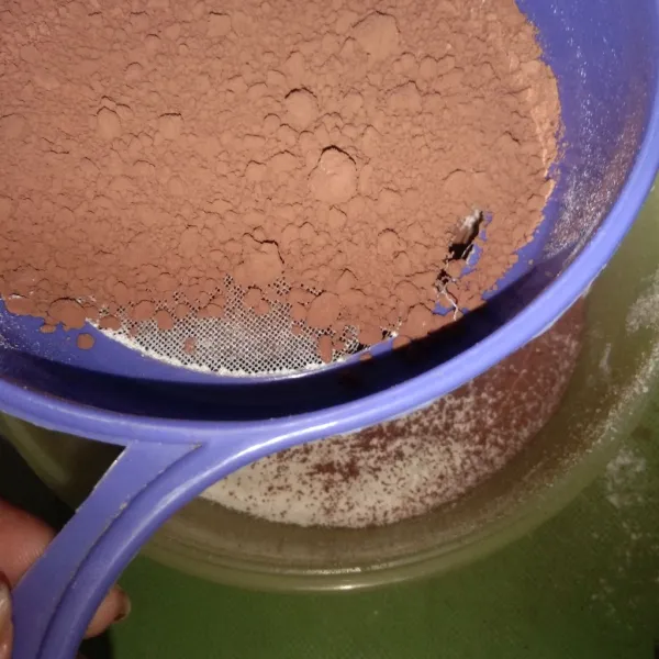 Dalam wadah lain, saring tepung terigu dan cokelat bubuk agar teksturnya lebih halus. Aduk rata