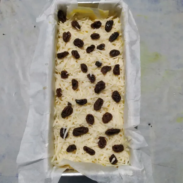Tuang adonan ke dalam loyang yang sudah dilapisi baking paper. Beri keju dan kismis. Hentakkan dua kali agar adonan padat