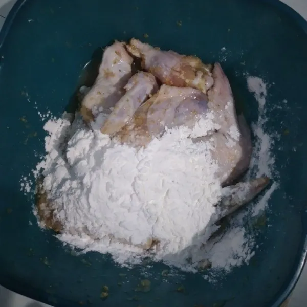 Tambahkan tepung tapioka ke dalam wadah berisi ayam yang sudah dimarinasi, lalu aduk merata
