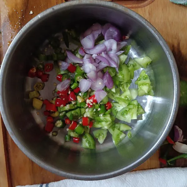 Siapkan wadah, campurkan irisan tomat hijau, cabai, dan bawang. Aduk merata.