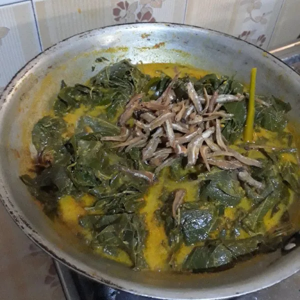 Setelah santan mendidih, masukkan daun singkong dan ikan teri goreng. Aduk merata hingga bumbu meresap.