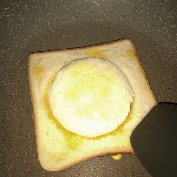 Tutup bagian telur yang masih basah dengan roti bulat. Setelah bagian bawah kecokelatan, balikkan.
