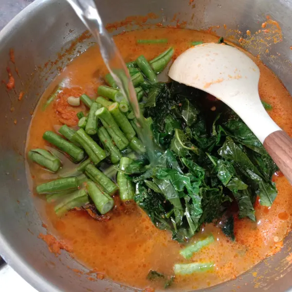 Masukkan potongan daun singkong rebus dan potongan kacang panjang. Tuangi dengan air secukupnya. Aduk rata.