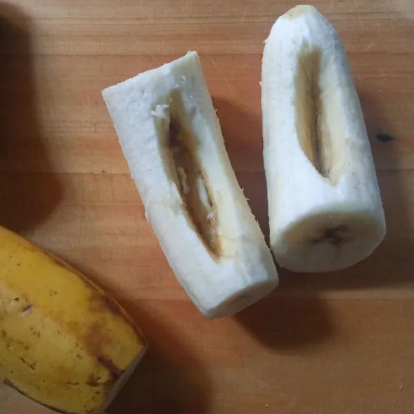Potong pisang menjadi dua bagian lalu kupas. Buat liang dengan bantuan ujung pisau.