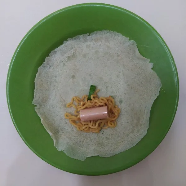 Potong sosis menjadi tiga bagian. Isi kulit lumpia dengan mie dan potongan sosis, lalu gulung. Rekatkan ujungnya dengan campuran air dan tepung terigu