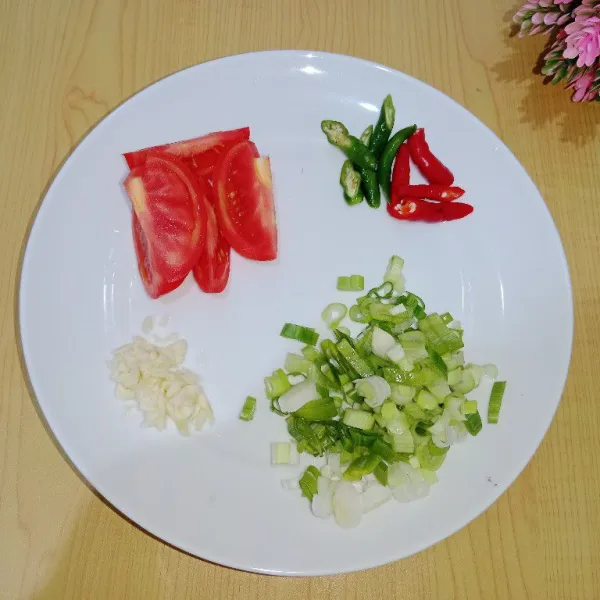 Siapkan semua bahan yang digunakan, kemudian cincang halus bawang putih, iris tipis daun bawang, iris serong cabai dan potong besar tomat merah.