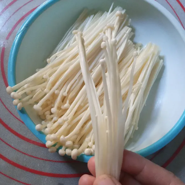 Potong akar jamur enoki tanpa membuka bungkus plastiknya. Keluarkan jamur enoki yang sudah bersih kemudian cuci dan peras ringan. Bagi jamur menjadi bongkahan kecil.