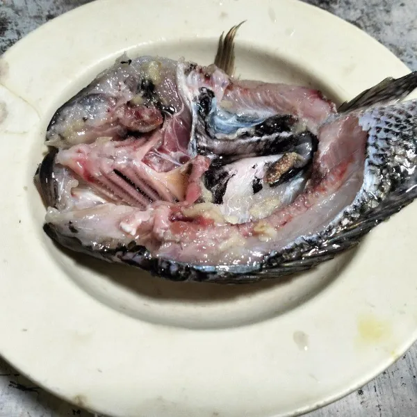 Cuci bersih ikan mujair, belah dua di bagian perut. Lumuri dengan bumbu bawang putih dan garam.