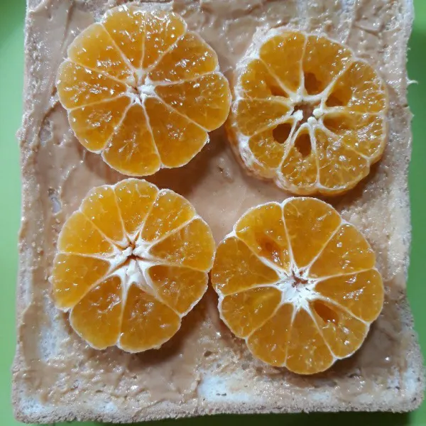 Susun potongan jeruk manis di atas sisi yang dioles selai kacang.