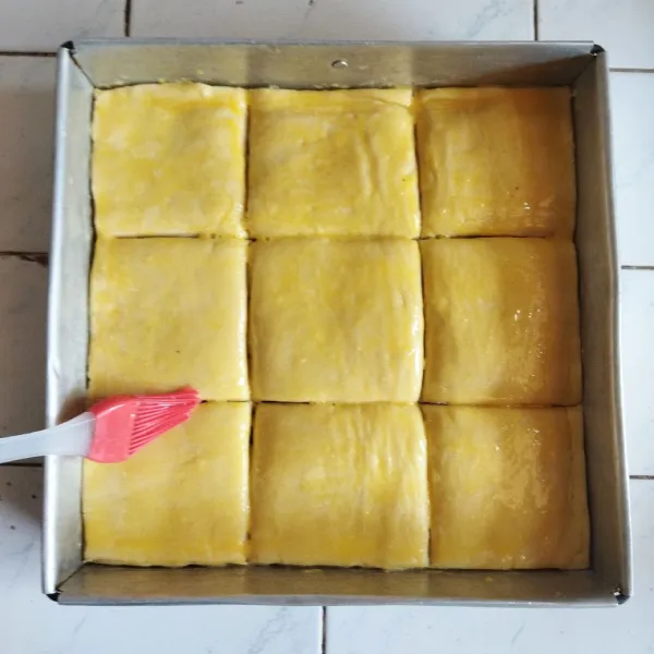 Potong puff pastry yang telah berlapis menjadi berbentuk kotak beberapa bagian. Setelah itu olesi dengan kuning telur pada bagian atasnya