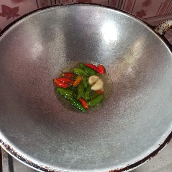 Panaskan minyak goreng secukupnya, kemudian masukkan cabai rawit dan bawang putih, goreng hingga setengah matang.