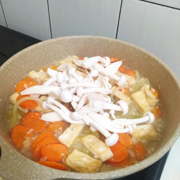 Masukkan wortel, tambahkan sedikit air lalu masak hingga wortel setengah matang. Masukan tahu dan jamur shimeji.