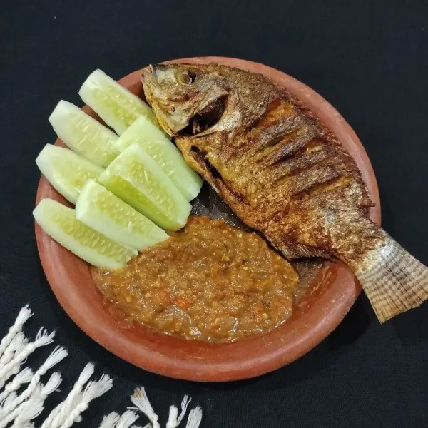 Sisihkan sambal terasi ke bagian tepi cobek. Lalu tata ikan goreng dan sajikan dengan lalapan timun.