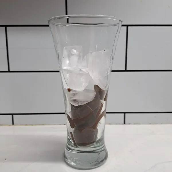 Potong dadu puding cokelat lalu masukkan ke dalam gelas saji. Tambahkan es batu secukupnya.