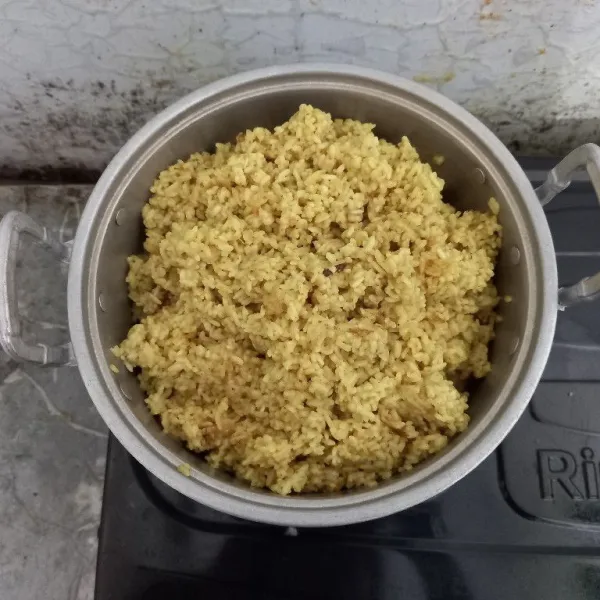 Masukkan beras yang setengah matang ke dalam kukusan panci. Kukus hingga menjadi nasi kuning yang matang.