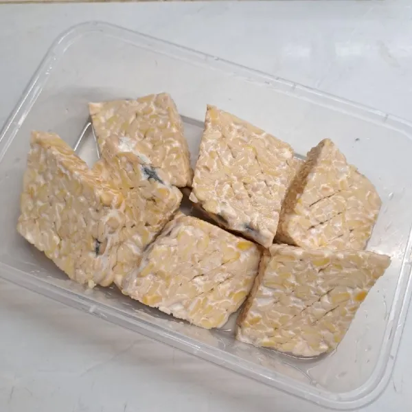 Iris tempe, lalu kerat-kerat. Rendam tempe dalam campuran larutan air dan garam sebentar saja