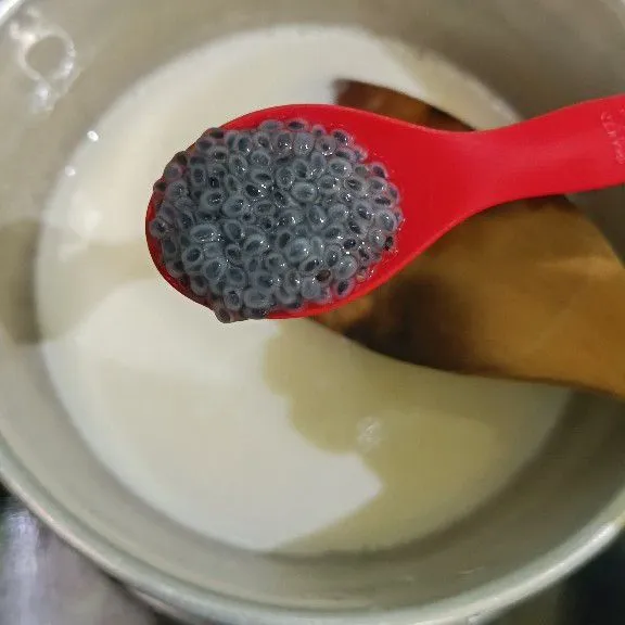 Selama menunggu, campur puding susu, bubuk jelly, susu cair, dan susu kental manis jadi satu, lalu aduk rata. Masak hingga mendidih dan matikan api kompor. Ambil sekitar 2-3 sendok teh biji selasih yang sudah diseduh, masukkan ke dalam puding susu, aduk rata.