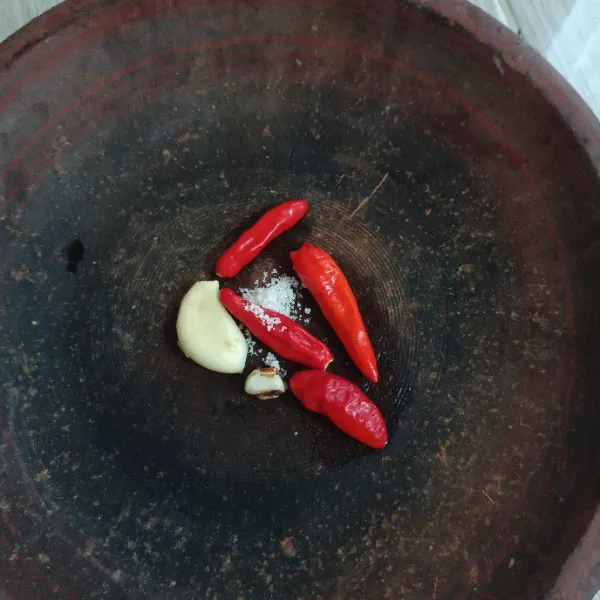 Kupas bawang putih dan cabut tangkai cabai serta kupas kencur. Masukkan dalam cobek bersama dengan garam dapur.