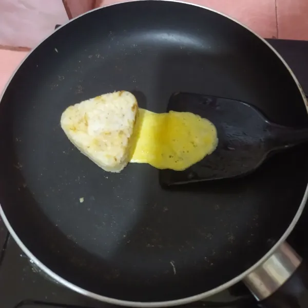 Kocok telur beri sejumput garam.
Panaskan pan anti lengket, olesi dengan sedikit minyak lalu sendokkan telur memanjang.
Selagi bagian atasnya masih basah, letakkan nasi kepal di atasnya.
