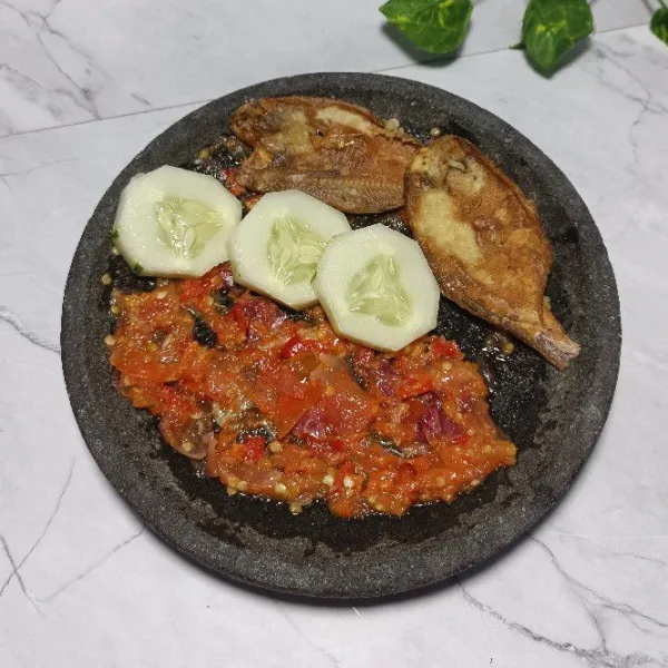 Tata ikan asin ke dalam cobek berisi sambal tomat dan beri lalapan seperti timun atau sesuai selera.