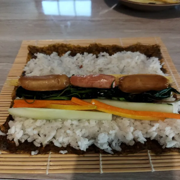 Siapkan nori diatas sushi mat beri 1/2 bagian nasi, lalu beri isian timun, wortel, bayam, sosis, dan telur dadar. Gulung dan padatkan.