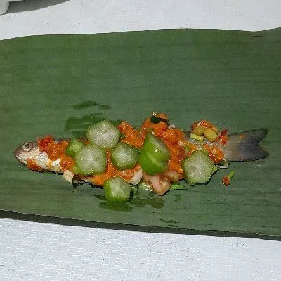 Ambil selembar daun pisang letakkan 1 ekor ikan lalu tambahkan potongan belimbing wuluh, kemudian gulung rapikan semat ke 2 ujungnya dengan lidi.