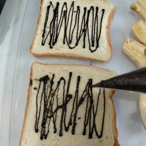 Beri glaze coklat di atas roti tawar.