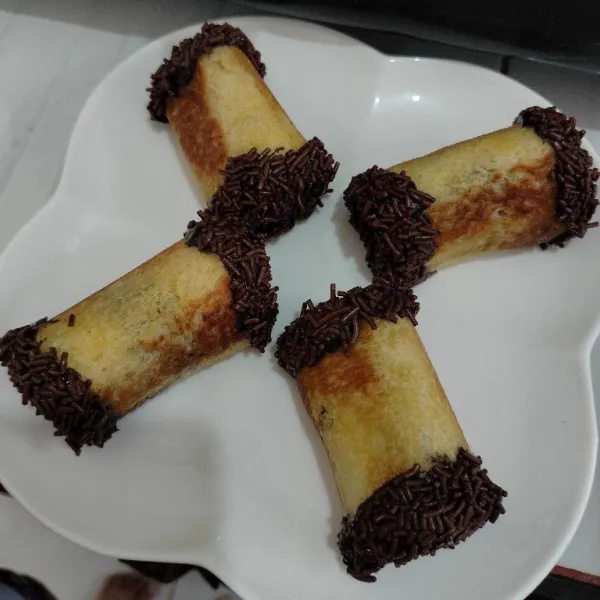 Kerat dua roti, lalu celupan bagian ujung roti ke dalam glaze cokelat lalu celupkan ke dalam meses. Tata di piring saji dan siap disajikan.