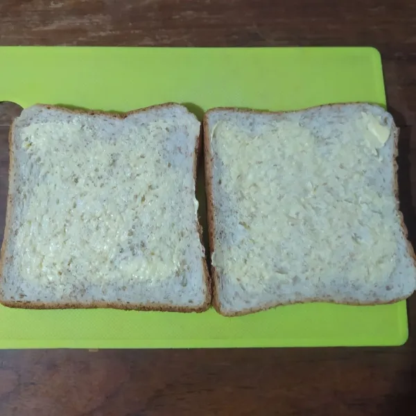 Oles salah satu sisi roti dengan margarin.