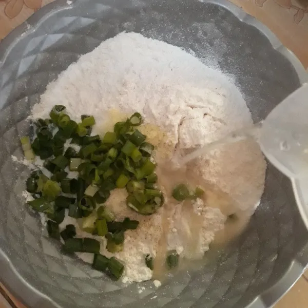 Tambahkan air rebusan bawang yang mendidih sedikit demi sedikit, aduk rata hingga kalis.