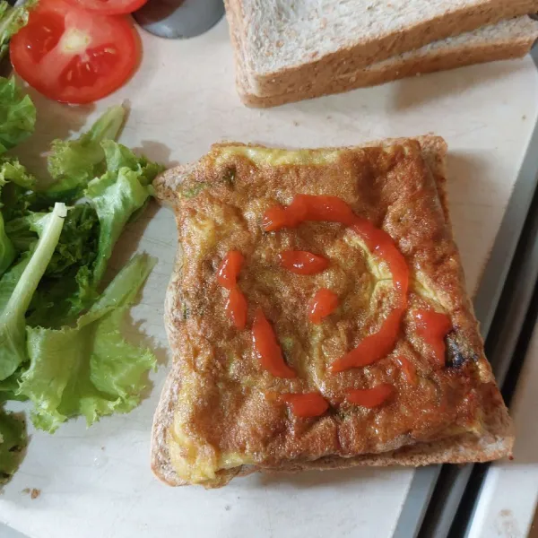 Timpa dengan telur. Beri saos, tutup dengan daun selada dan terakhir tutup dengan lembaran roti satunya lagi.