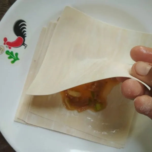Ambil selembar kulit pangsit, beri 1 sdm adonan telur kemudian beri air di sekeliling kulit pangsit dan tumpuk dengan kulit pangsit dan rekatkan.