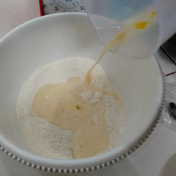 Campurkan bahan B ke dalam gelas, aduk merata lalu tuang ke dalam adonan tepung, uleni perlahan hingga kalis.