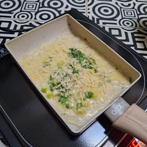 Panaskan pan, beri olesan tipis minyak goreng. Tuang 1 sendok sayur adonan telur. Beri taburan keju parut lalu masak sampai berkulit bagian bawahnya.