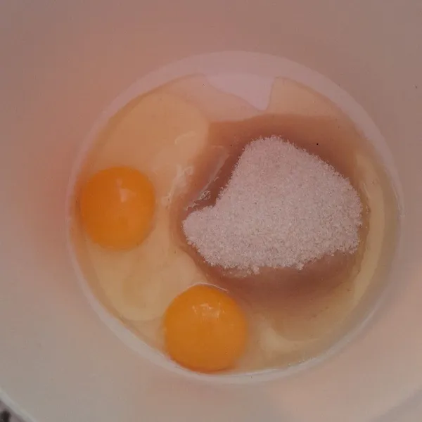 Dalam wadah, pecahkan telur dan tambahkan gula.
