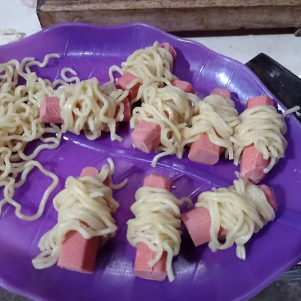 Potong sosis jadi 2 lalu kerat bagian atasnya, gulungkan mie ke sosis, lakukan sampai selesai.