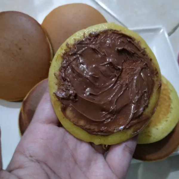Ambil selembar dorayaki, lalu beri isian selai cokelat yang cukup banyak di bagian tengah. Tutup dengan dorayaki lagi. Sajikan.