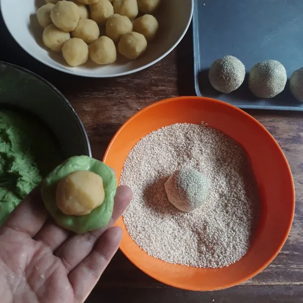 Ambil secukupnya adonan kulit, pipihkan, isi dengan isian kacang hijau, bulatkan. Gulingkan di atas wijen hingga rata. Lakukan sampai adonan habis.