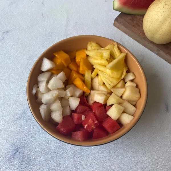 Kupas dan potong-potong semangka, nanas, mangga, apel dan pir. Masukkan ke dalam mangkuk.