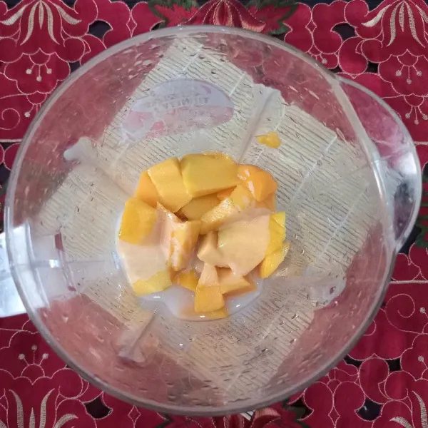 Kupas mangga dan potong dadu ukuran besar. Blender satu buah mangga dengan krim kental manis bersama air 150 ml hingga halus.